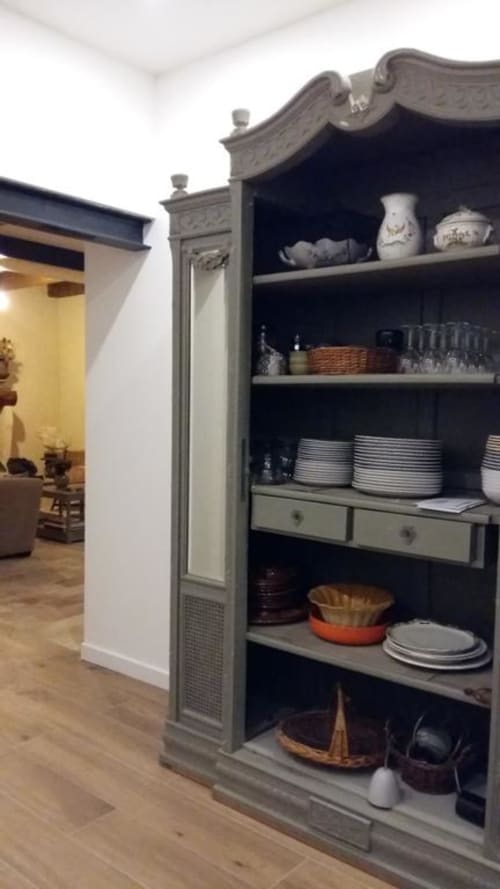 Elegant kitchen cabinet with decorative Asian-inspired top displaying dinnerware and household items at Mas des Artistes