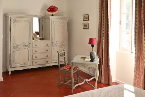 Elegant bedroom at Mas des Artistes cottage with cream wardrobe, writing desk, red tile flooring, and garden views through