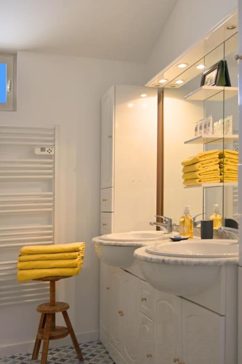 Modern bathroom at Mas des Artistes cottage with dual white sinks, large mirror, yellow towels, and heated towel rack in