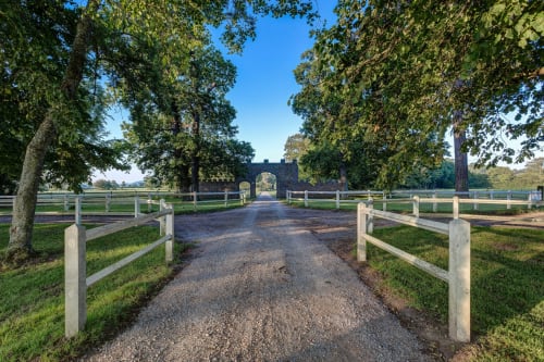 Tree-lined gravel driveway leading to historic stone gatehouse at Château d'Alexis de Tocqueville in Normandy France