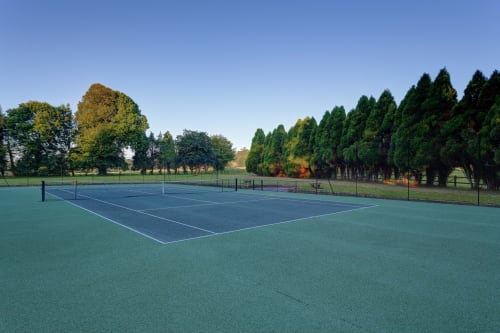 Tennis court at Château d'Alexis de Tocqueville with tree-lined grounds and clear sky