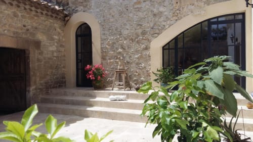 Rustic stone courtyard at Mas des Artistes in Mouriès with arched doorway, flowering plants, and terracotta tiles