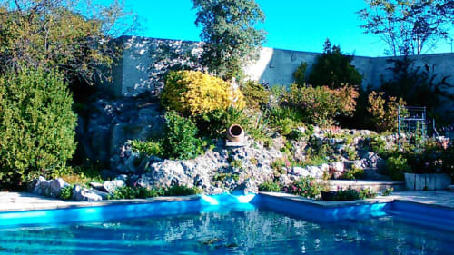 Turquoise pool at Mas des Artistes BnB in Mouriès, France, surrounded by rocky landscape and flowering plants