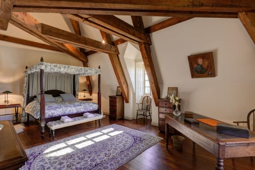 Chambre élégante aux poutres apparentes du Château d'Alexis de Tocqueville, lit à baldaquin violet et mobilier d'époque
