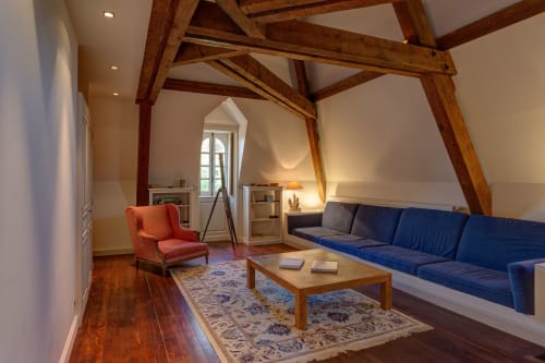 Suite élégante sous les combles du Château d'Alexis de Tocqueville avec poutres apparentes, canapé bleu et mobilier d'époque