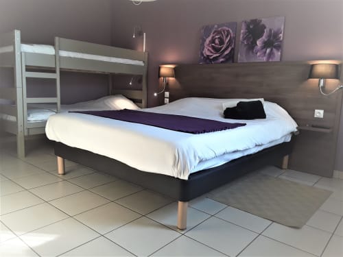 Spacieuse chambre quadruple au Relais Motel de Maisonnay avec lit queen-size, lits superposés, œuvres florales violettes et équipements modernes