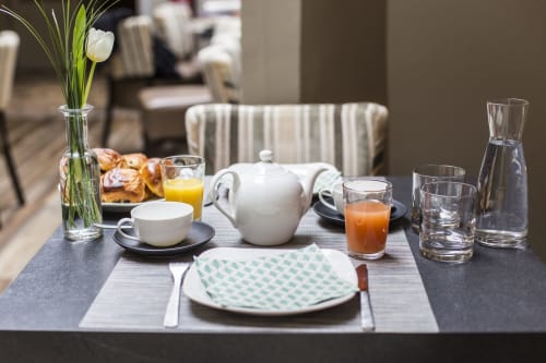 Table de petit-déjeuner élégante à l'hôtel Les Cabines à Houlgate avec tulipes blanches, théière, jus et assiette aux motifs.