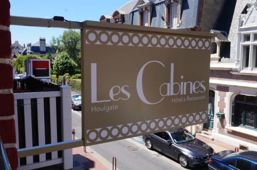 Enseigne de l'hôtel Les Cabines à Houlgate avec auvent beige, voitures garées et bâtiments en brique