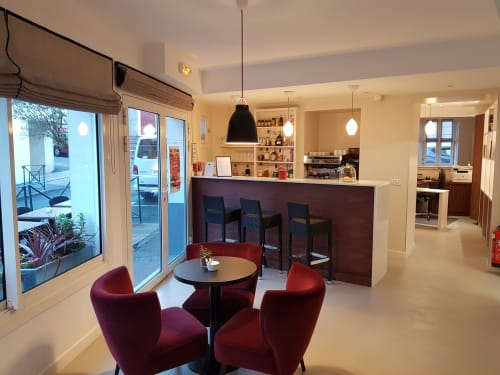 Hotel Au Bon Coin lobby in Biarritz with red armchairs, bar counter, and modern pendant lighting