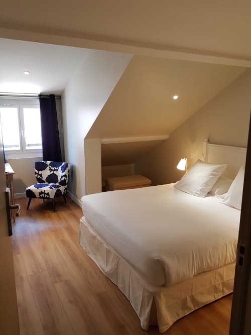 Spacious attic bedroom at Hotel Au Bon Coin in Biarritz with queen bed, blue patterned chair, and wooden flooring