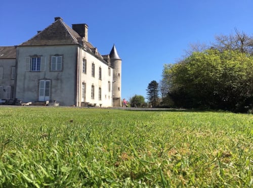 Château d'Asnières en Bessin, un manoir de pierre charmant avec tour, niché dans des jardins soignés sous un ciel bleu dégagé