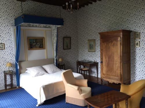La chambre bleue du Château d'Asnières en Bessin propose un lit à baldaquin, une armoire en bois et un papier peint à motifs bleus