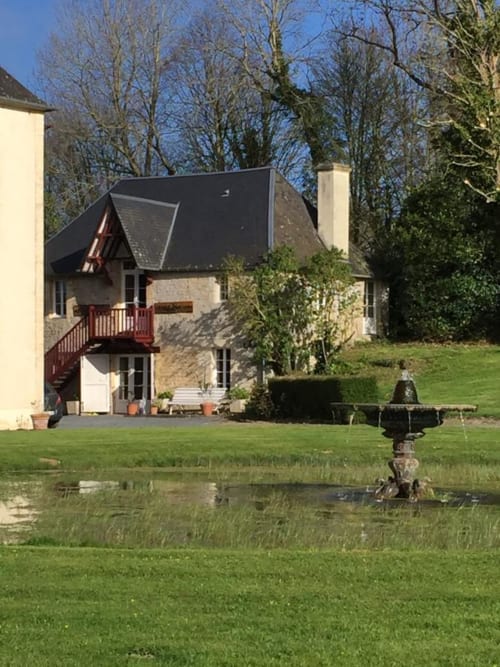 Private cottage at Chateau d'Asnieres en Bessin with dark roof, red deck, manicured gardens and ornamental pond in Normandy