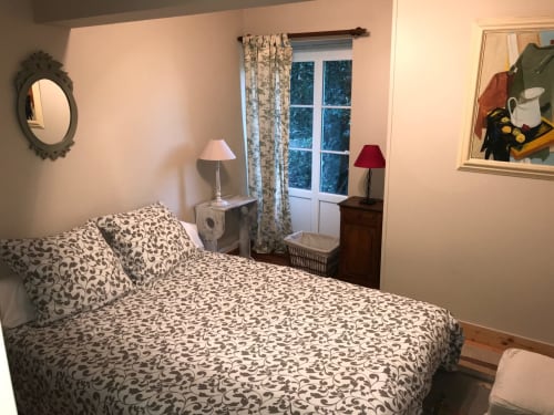 Cozy bedroom in Chateau d'Asnieres cottage with patterned bedding, nightstands, desk lamp, and garden view windows