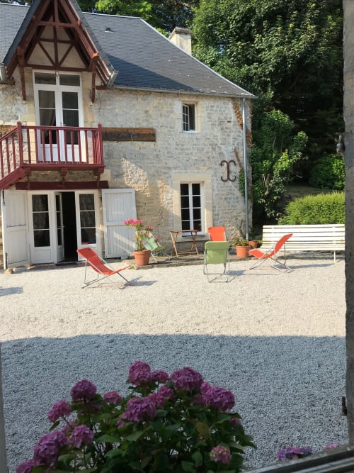 Chateau d'Asnieres en Bessin private cottage with red deck, stone facade, and garden seating area in Normandy, France