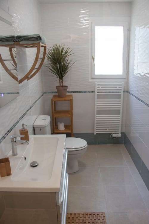 Modern bathroom at Belloréade B&B in Belloc with white tiles, sink, toilet, heated towel rack, and potted plant by window