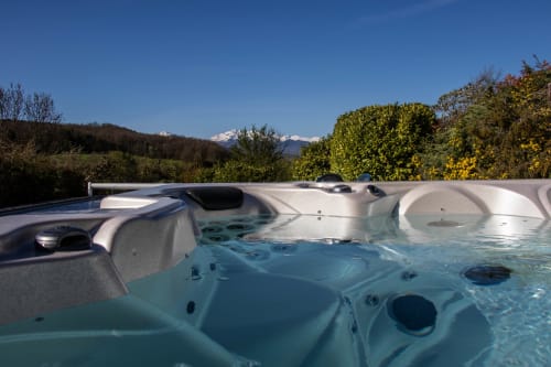 Outdoor hot tub with turquoise water at Belloréade in Belloc, snowy mountains and gardens in background