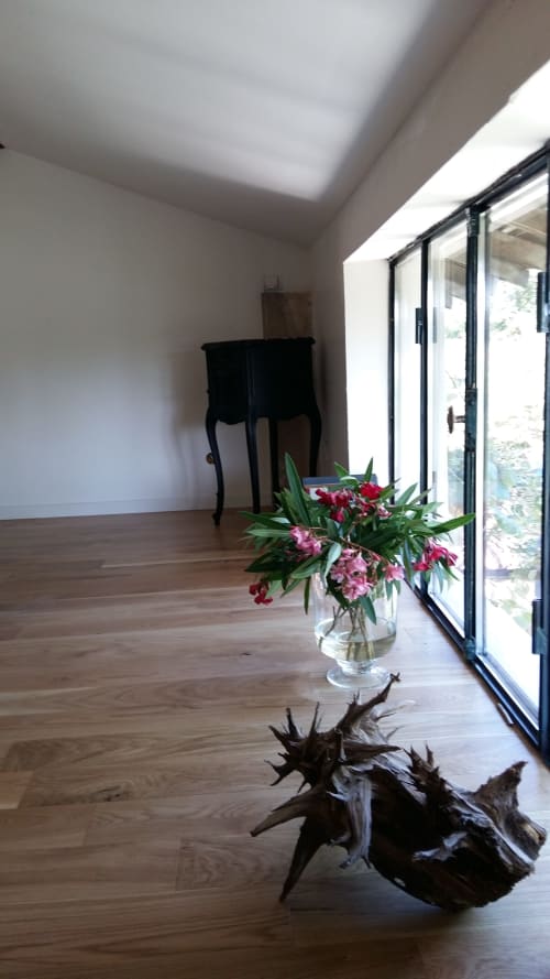 Bright cottage interior at Mas des Artistes with wooden floors, pink flowers, and black furniture overlooking garden