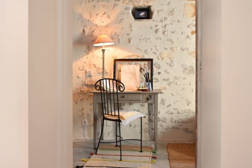Cozy work nook in Mas des Artistes cottage with desk, lamp, and black chair against rustic stone wall