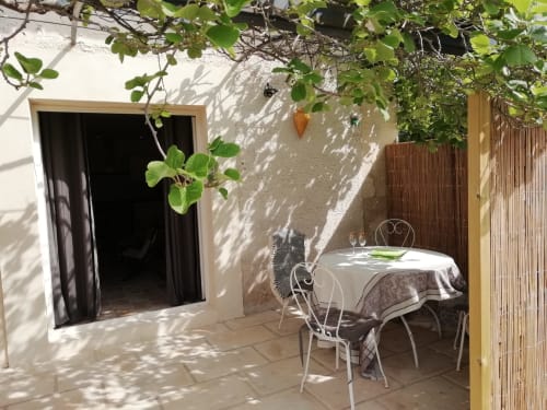 Terrasse de jardin ombragée de la maison Mas des Artistes avec table à manger, chaises blanches et vignes grimpantes à Mouriès