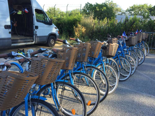 Row of blue bikes with brown baskets at Saint Martin B&B in Ollioules, France, with van and lush greenery nearby