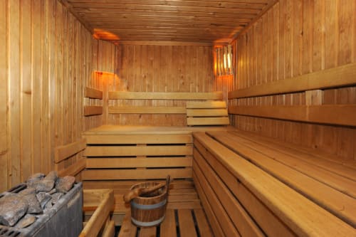 Traditional wooden sauna with tiered benches, bucket, and heated rocks at Hotel Residence Europe & Spa in Clichy