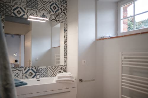 Salle de bain moderne du B&B Le Pignié avec carrelage à motifs, lavabo, miroir et vue sur le jardin de Lescure-d'Albigeois