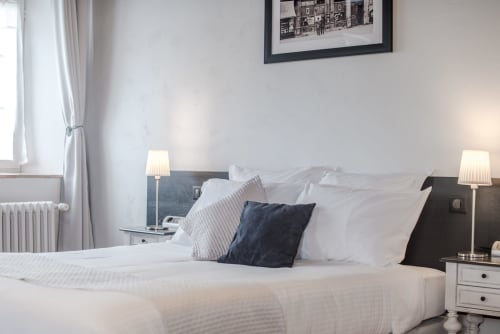 Chambre lumineuse au Gîte Le Pignié à Lescure-d'Albigeois avec literie blanche, tête de lit sombre, lampes jumelées et art mural encadré