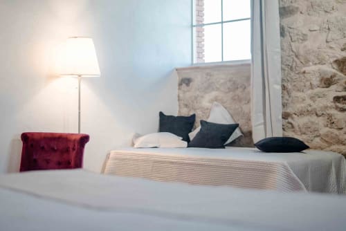 Chambre moderne au gîte Le Pignié à Lescure-d'Albigeois avec murs en pierre, lit aux oreillers noirs, fauteuil bordeaux et sol