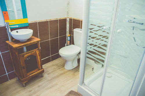 Salle de bain moderne du gîte Angkor avec vasque blanche, toilettes, douche à l'italienne et mur d'accent en carrelage brun
