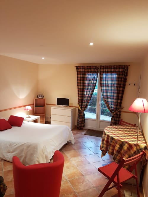 Spacieuse chambre studio avec lit blanc, mobilier rouge, rideaux à carreaux et vue sur jardin à La Croix De La Jarrie, Châtres
