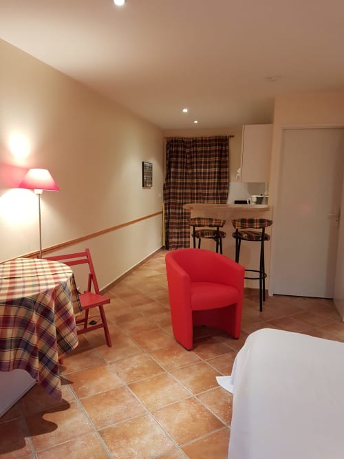 Studio à La Croix De La Jarrie avec fauteuil rouge, table à manger, kitchenette équipée et carrelage en terre cuite