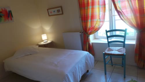 Gemütliches Schlafzimmer in La Croix De La Jarrie, Châtres mit weißem Bett, Nachttischlampe, blauem Sessel und farbenfrohen Vorhängen