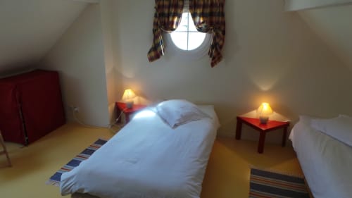Gemütliches Dachzimmer im La Croix De La Jarrie mit Einzelbetten, roten Nachttischen und rundem Fenster mit Gartenblick