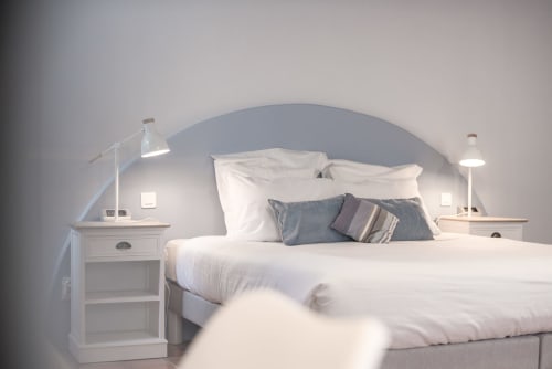 Bright modern bedroom at Le Pignié gîte with arched headboard, white bedding, and gray accents