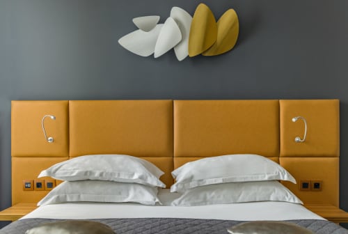 Modern hotel bedroom at Residence Europe & Spa with mustard yellow padded headboard, white pillows, and wall art