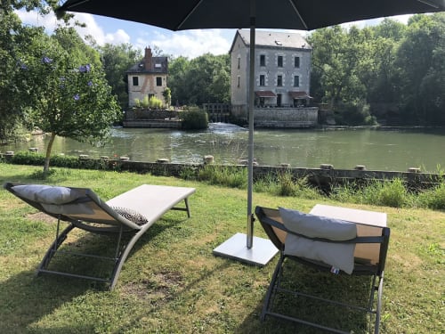 Espace de détente en bord de rivière au Moulin De La Chevrière à Saché, avec les bâtiments historiques du moulin de l'autre côté de l'eau