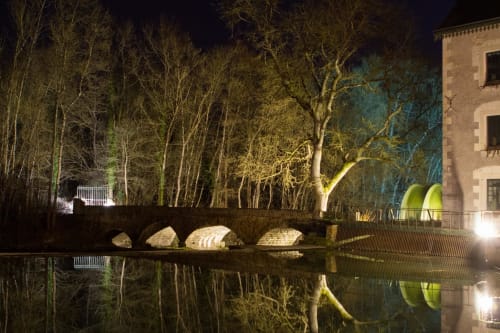 Le Moulin de la Chèvrière illuminé la nuit, ses arbres se reflétant dans l'eau calme de Saché
