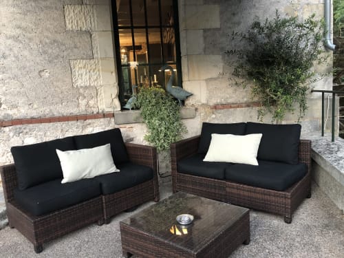 Espace de détente extérieur au Moulin De La Chevrière avec canapés en rotin, coussins noirs et plantes en pots à Saché, France