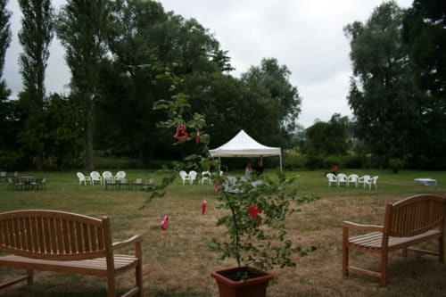 La Chatellenie garden setup with wooden benches, potted roses, white tent, and chairs on lawn in Saint Aubin le Cauf