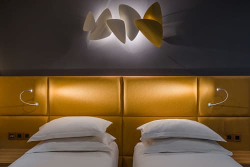 Modern hotel bedroom at Residence Europe & Spa in Clichy with twin beds, gold headboard, and sculptural ceiling fixture