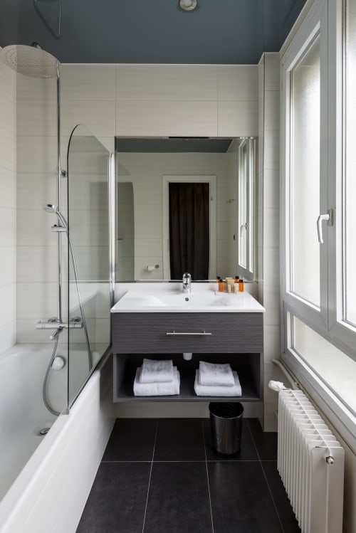 Modern bathroom at Hotel Residence Europe & Spa in Clichy with vanity, shower, and dark tile flooring