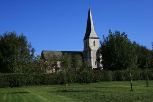 Church with tall steeple surrounded by green hedges and lawn at La Chatellenie B&B in Saint Aubin le Cauf, France