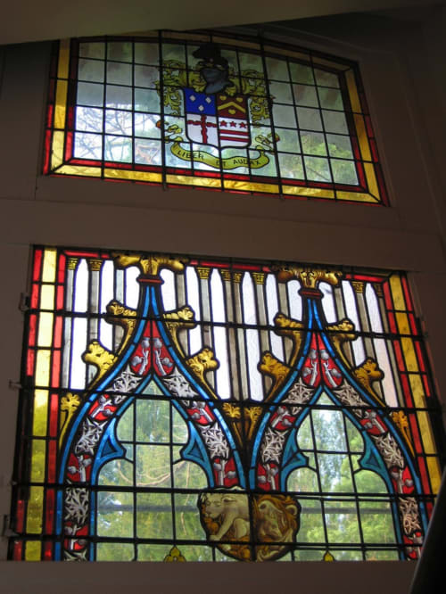 Ornate stained glass windows at La Chatellenie B&B in Saint Aubin le Cauf, featuring heraldic crests and decorative patterns