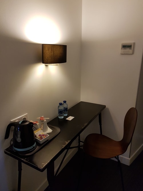 Modern hotel desk with kettle, water bottles, and brown chair under wall lamp in Biarritz hotel room