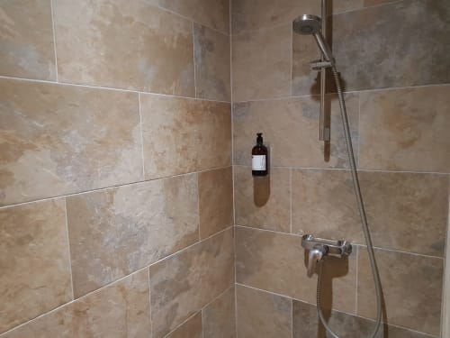 Modern shower in Hotel Au Bon Coin's Twin Room, Biarritz, with beige tiled walls, rainfall showerhead, and amenities shelf