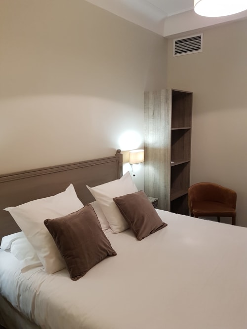 Chambre d'hôtel moderne à l'Hôtel Au Bon Coin, Biarritz, avec lit, coussins marron, lampe de chevet, étagères en bois et plafond