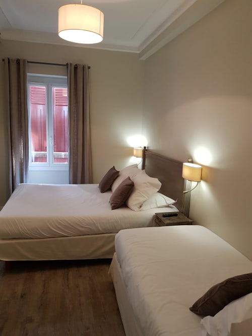 Chambre quadruple à l'Hôtel Au Bon Coin à Biarritz avec deux lits, éclairage moderne et portes-fenêtres avec vue sur la ville