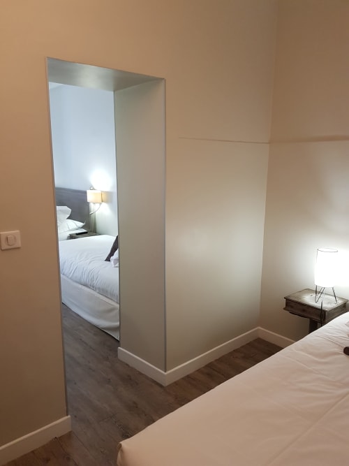 Chambre moderne de l'Hôtel Au Bon Coin à Biarritz avec cloison en verre dépoli séparant les zones de couchage dans une chambre quadruple