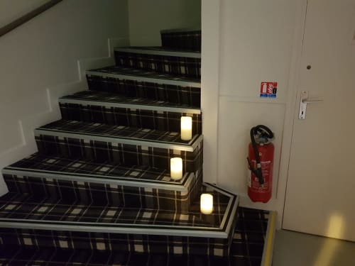 Illuminated staircase with plaid carpet pattern at Hotel Au Bon Coin, Biarritz, with fire extinguisher and emergency signs
